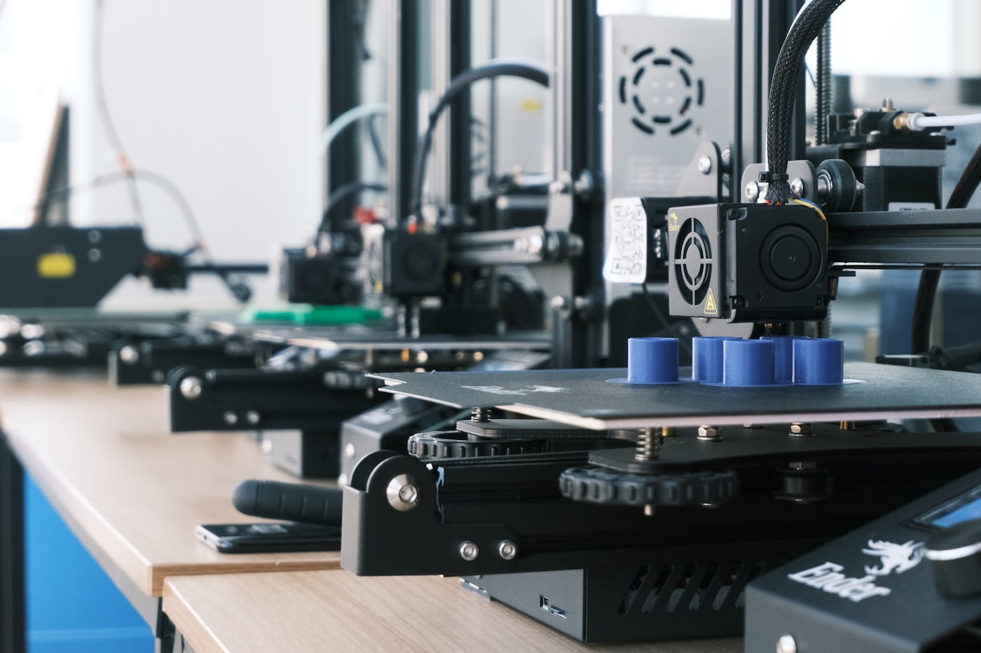 Fileira de impressoras 3D trabalhando lado a lado na bancada do ateliê