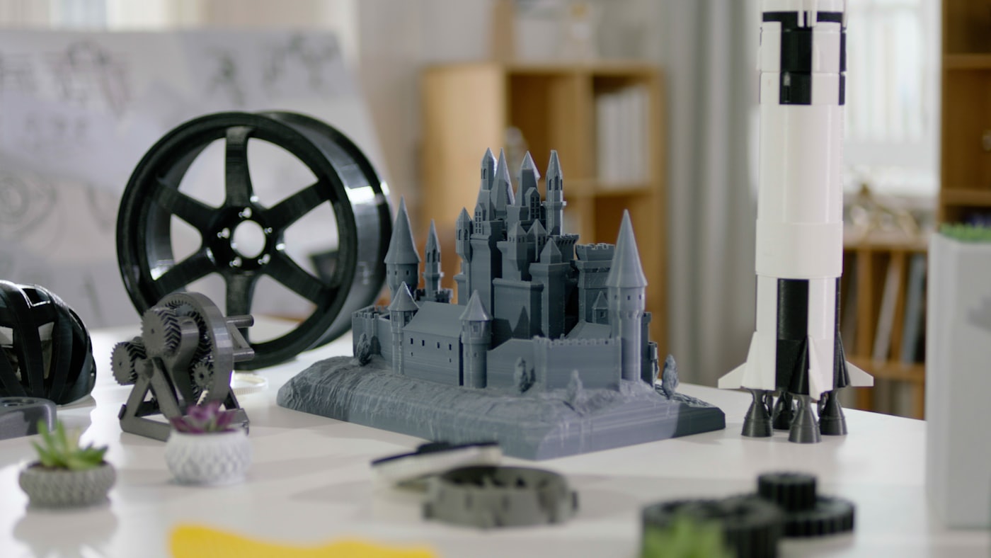 Peças impressas em 3D sobre a mesa: um castelo, uma roda, um foguete e engrenagens